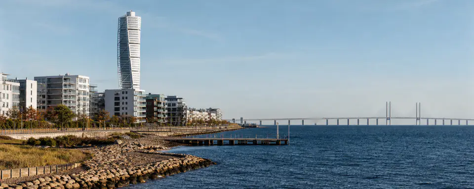 Illustrerad kustvy över Malmö med modern höghusbebyggelse, strandpromenad och Öresundsbron i klart dagsljus