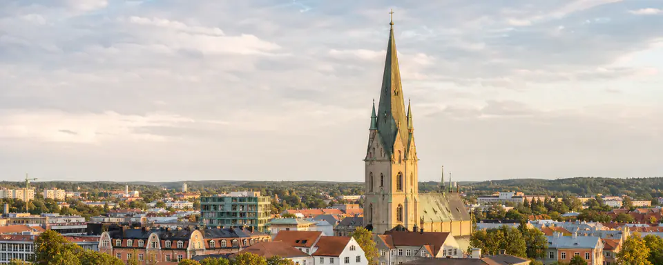 Illustrerad vy över Linköping med domkyrkans höga torn, historiska kvarter och grönskande stadsmiljö i kvällsljus